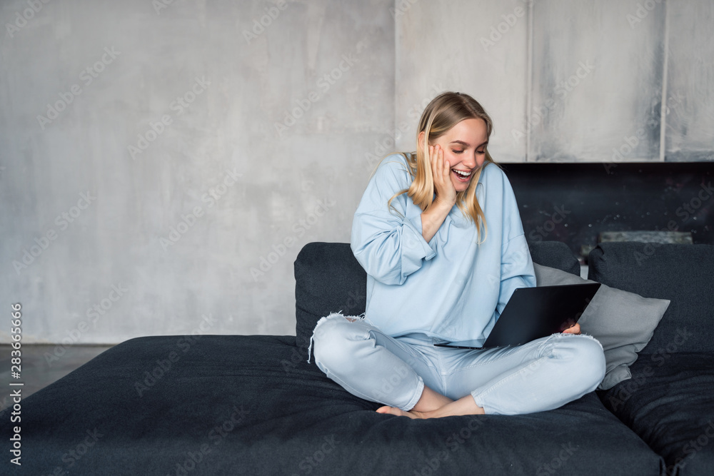 Image of happy woman using silver laptop while sitting on sofa
