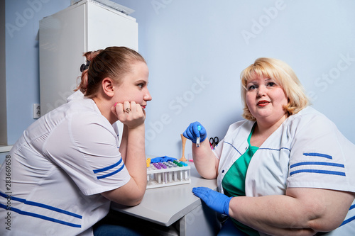 Experienced doctor fat woman and aspiring young doctor sittins at the table and discussing the medical problems