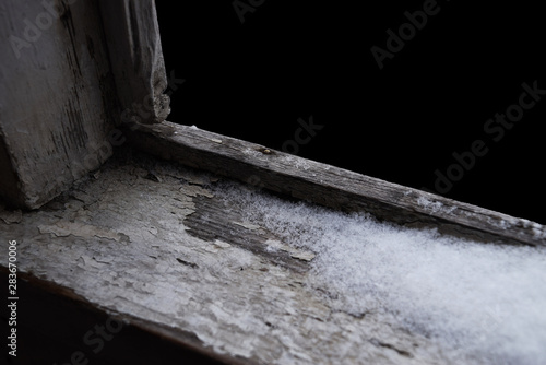Old shabby wooden windowsill partially covered with snow, isolated on black. Graphic element. Stage for objects or products.