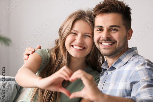 Portrait of happy loving couple holding hands in shape of heart at home