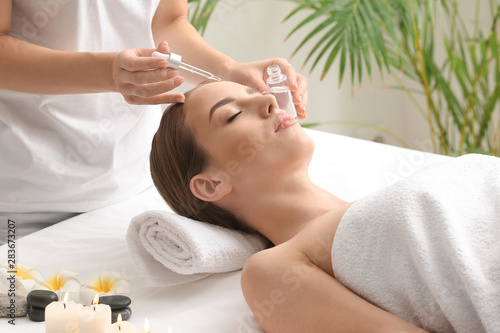 Beautiful woman undergoing treatment with face serum in beauty salon