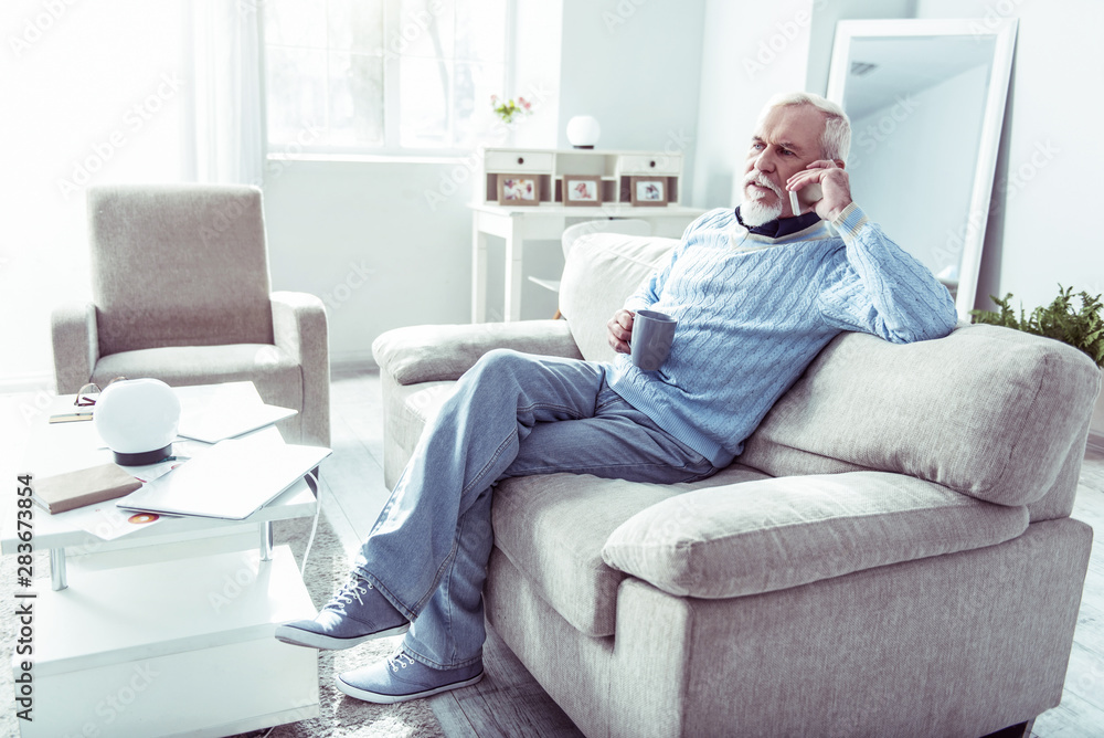 Obraz premium Stylish retired man holding his phone while calling wife from home