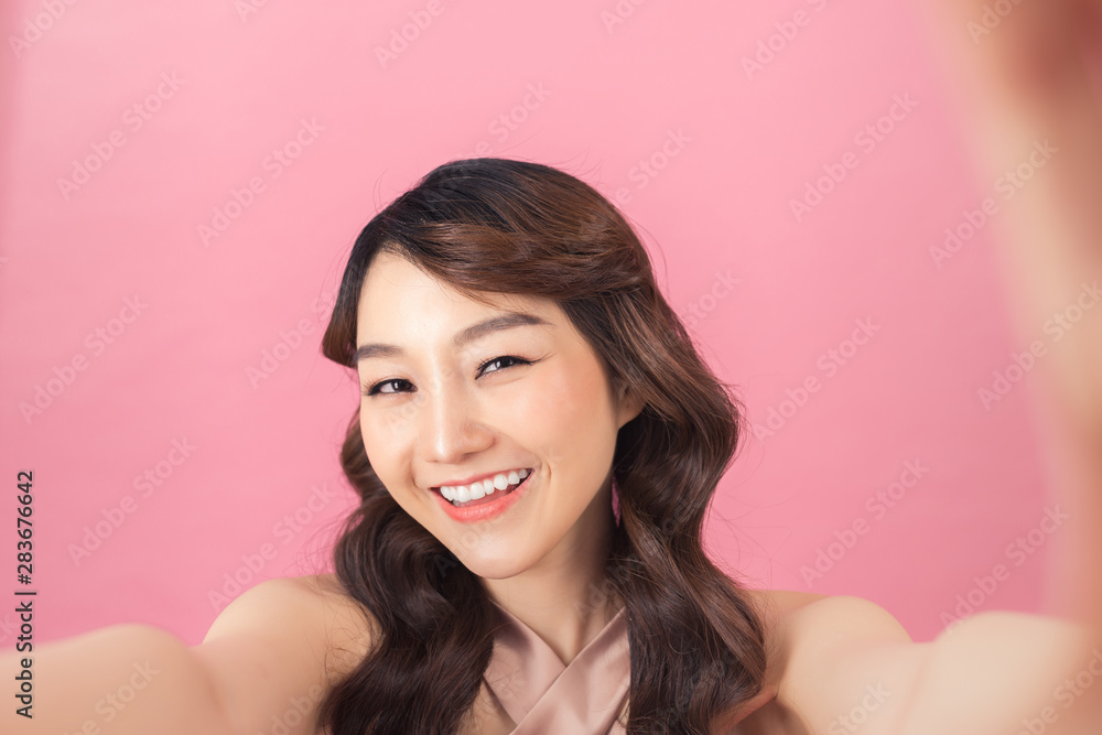 Studio portrait of beautiful woman smiling with white teeth and making selfie, photographing herself over pink background Studio portrait of beautiful woman smiling with white teeth and making selfie, photographing herself over pink background