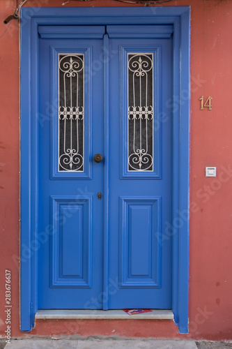 Blue wooden door with two small windows. Terracotta wall. Number plate next to the door. © Marija Krcadinac