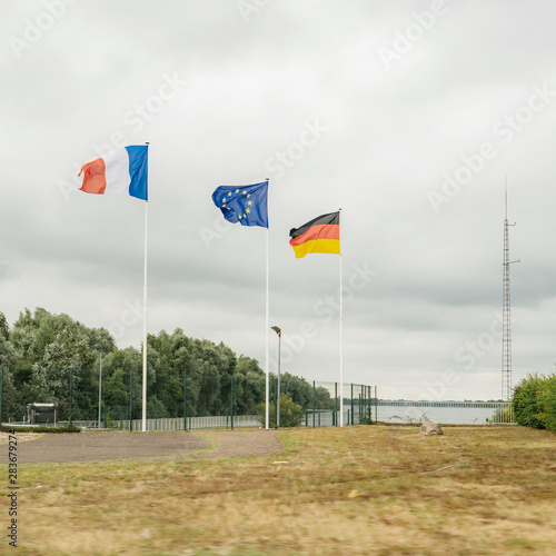 French, European union and German flags waving near the border between the two countries symbolizing friendship and fraternity
