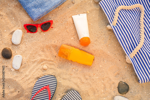 Bag with sunscreen cream, sunglasses and flip-flops on sand beach