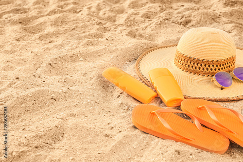 Hat with sunscreen cream, flip-flops and sunglasses on sand beach