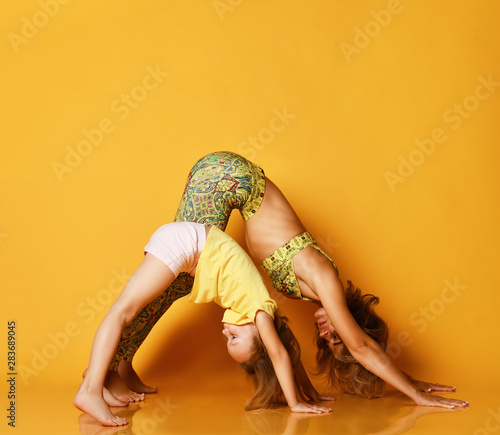 Young mother and daughter doing yoga exercises together in a fitness studio on a yellow background
