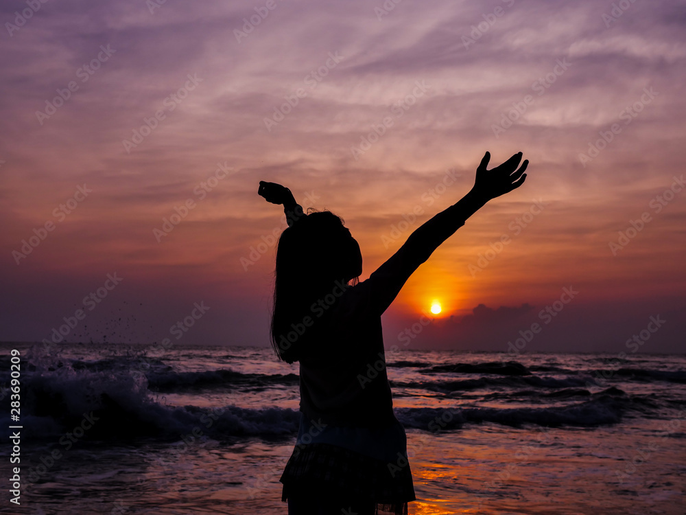 Girl raising hands with sun rise on the beach background.
