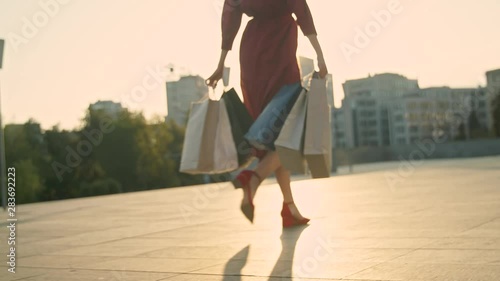 Young woman in red dress with shopping bags walks on the street during sunset