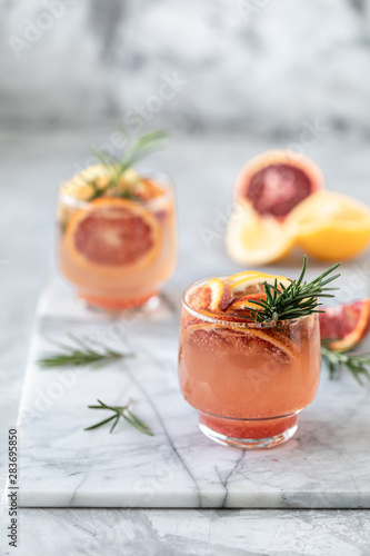Juice, water, cocktail with red orange and lemon and a rosemary branch on white marble
