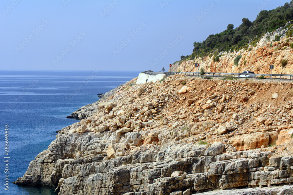 A white bus moves along a mountain road winding along the Mediterranean Sea. The concept is bus travel.