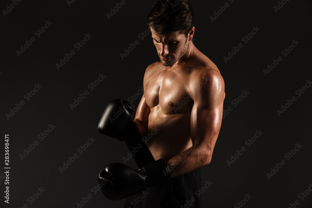 Concentrated strong handsome young sportsman boxer in gloves posing isolated over black wall background.