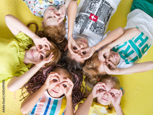 Group of beautiful cheerful children lie on their back looking at the camera on a yellow background