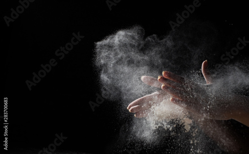 woman chef hand clap with splash of white flour and black background with copy space. © pavel siamionov