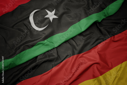 waving colorful flag of germany and national flag of libya.