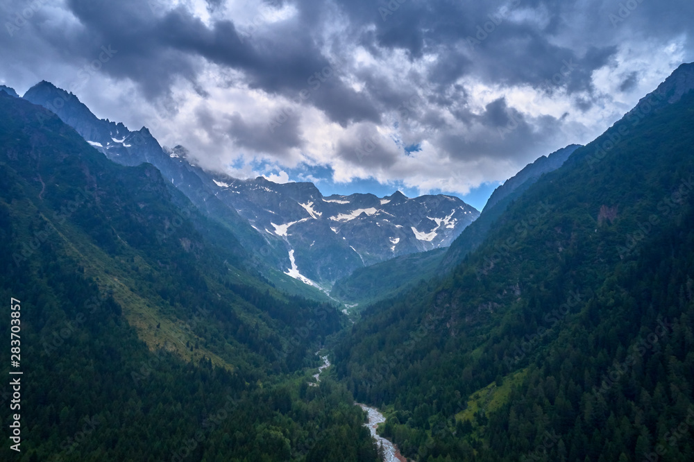 Naklejka premium Widok na górską rzekę. Rzeka spływa po zboczu na tle alpejskich gór w śniegu. Popularny kurort narciarski Ponte di Legno. Zdjęcie zrobione dronem.