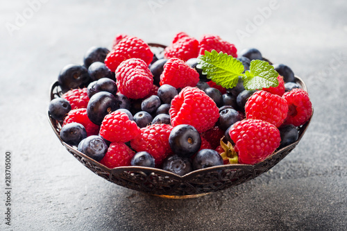 Fresh raspberries and blueberries in plate on dark background. Copy space.