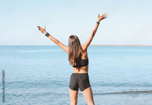 Young slim athletic long hair happy woman in sportswear doing exercises on the sea beach in the morning, healthy lifestyle
