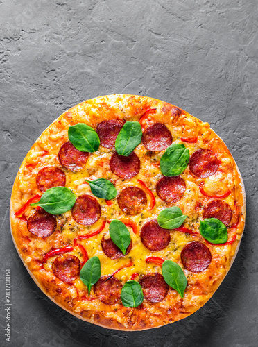Pepperoni Pizza with Mozzarella cheese, salami, pepper, Spices and Fresh spinach. Italian pizza on Dark grey black slate background
