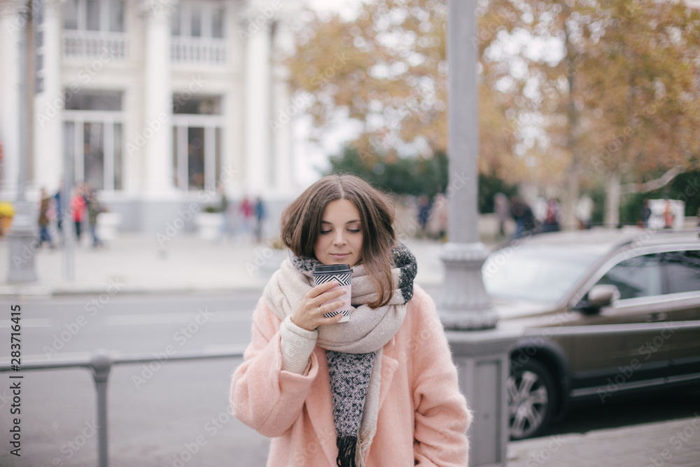Woman in pink trendy coat drinking coffee on street. 