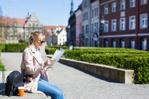 summer and travel concept - woman in sunglasses with map, backpack and camera in old town of Tallinn, Estonia