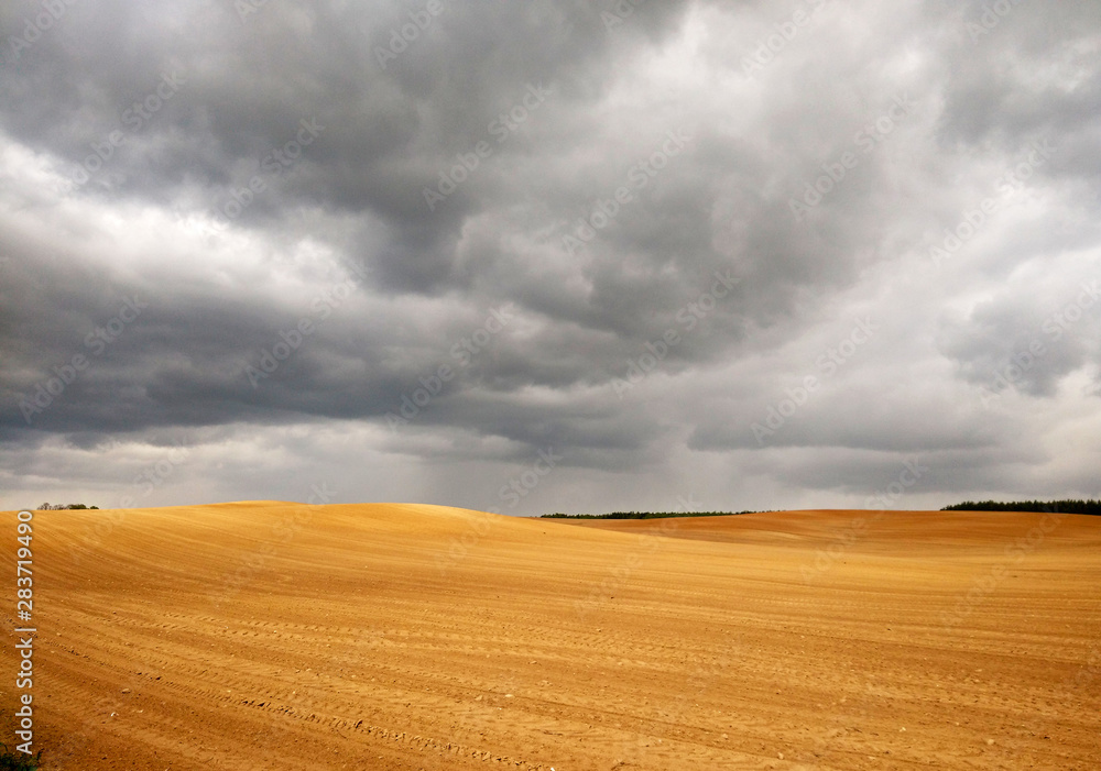 Dark stormy clouds over wheat harvested field. Empty yellow field with dramatic rainy clouds on the background.