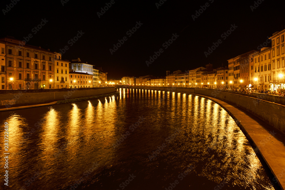 Golden lights on the Arno river shore in the old town of Pisa at night, outdoor summer nightlife with bars used by young people and tourists, copy space