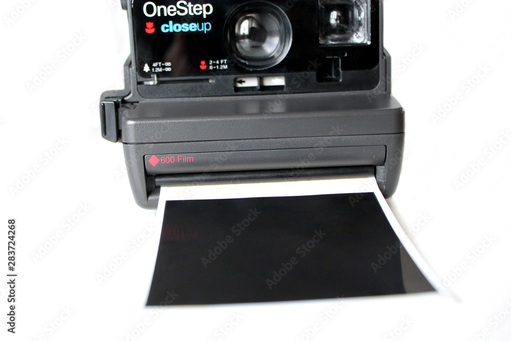 Retro polaroid instant camera isolated on white background with empty film going out. Black polaroid closeup. Old photography equipment Retro polaroid instant camera isolated on white background with empty film going out. Black polaroid closeup. Old photography equipment