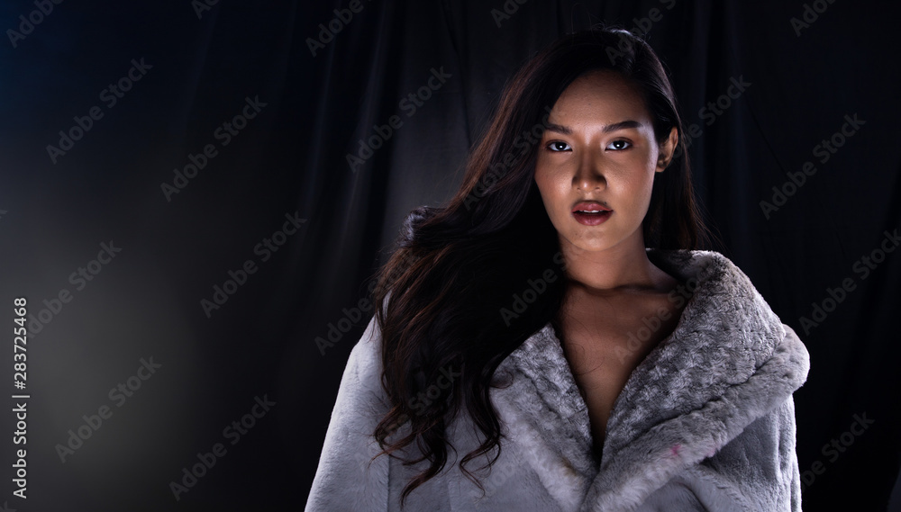 Portrait Fashion Beautiful Asian Woman make up attractive glam in fur coat and long curl black hair. Studio Lighting dark Background with smoke