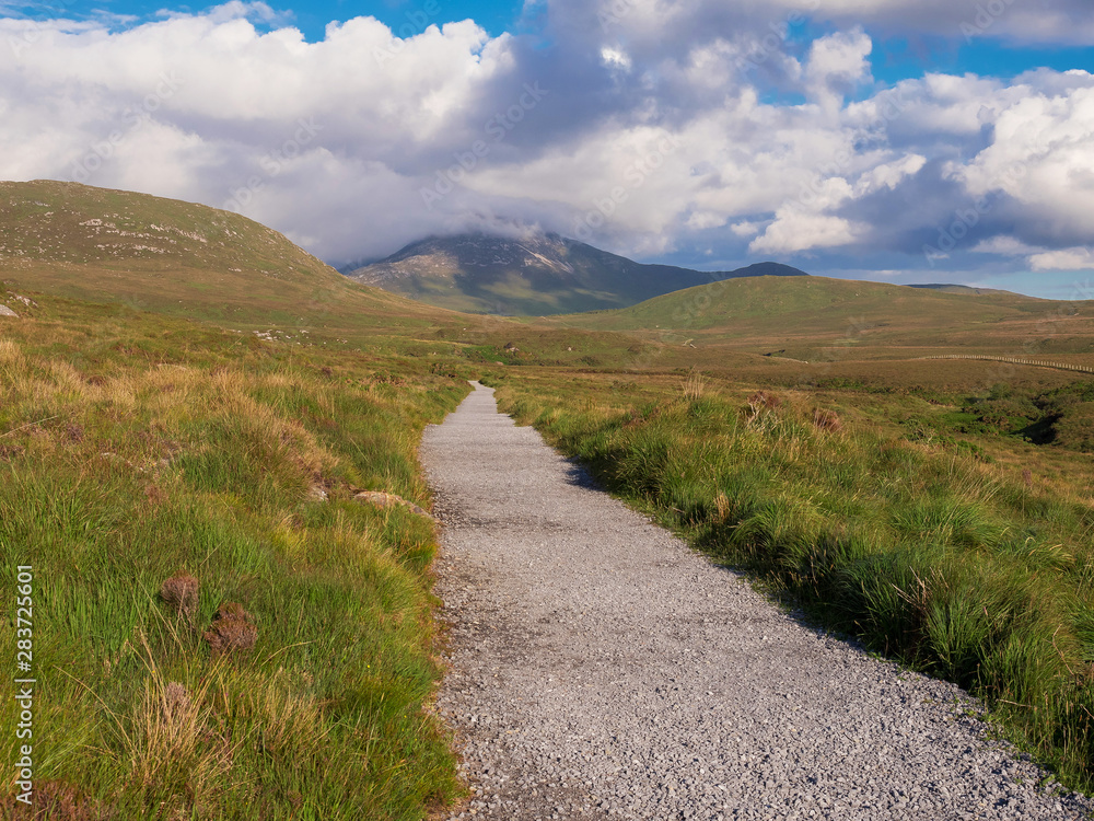 Walk path into mountains, Connemara National park, Ireland, Sunny warm day, Cloudy sky.