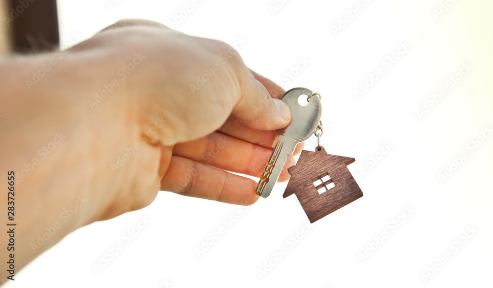 Obraz premium The mental key from door with wooden trinket in shape of house in man's hand in front of sky