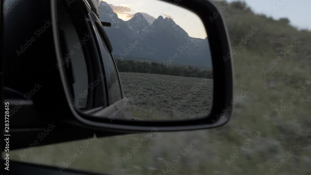 Grand Tetons at sunset view in side mirror of car while driving Grand Tetons at sunset view in side mirror of car while driving