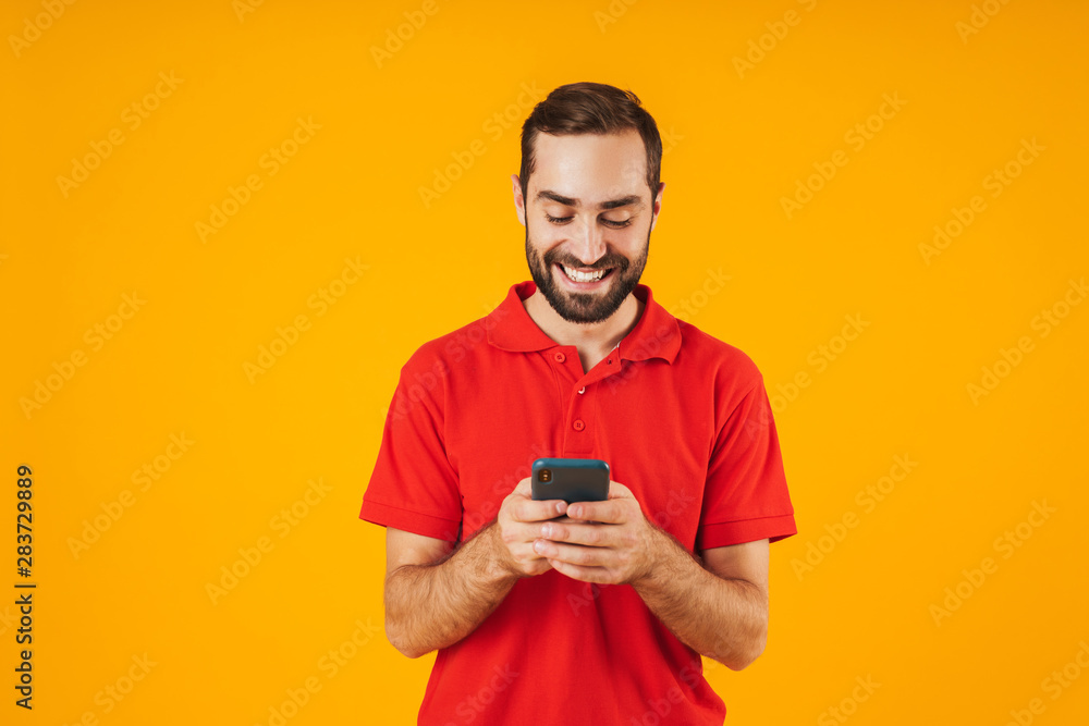 Portrait of joyful man in red t-shirt smiling and holding smartphone Portrait of joyful man in red t-shirt smiling and holding smartphone