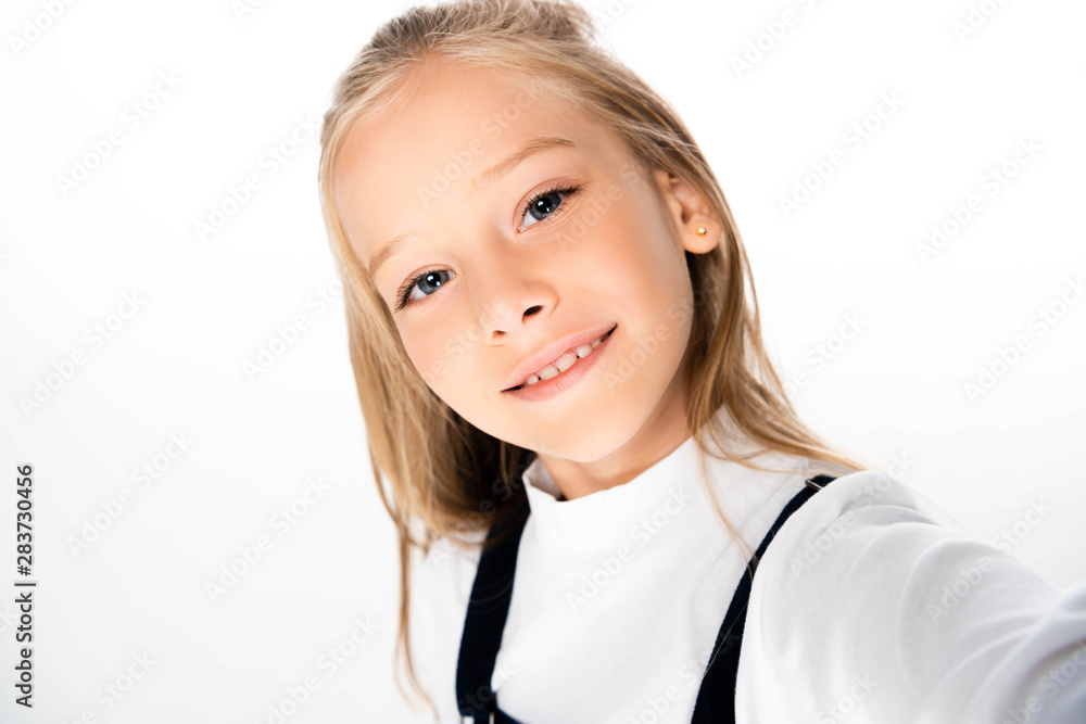 cheerful schoolgirl smiling at camera while taking selfie on white background cheerful schoolgirl smiling at camera while taking selfie on white background