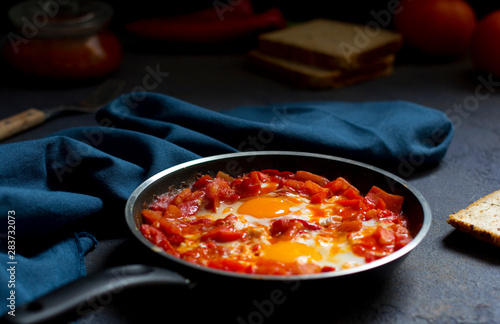 Shakshouka or shakshuka, eggs in a sauce of tomatoes and peppers, dark blue background, copy space for your text