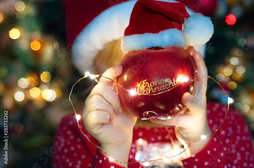 hands holding an apple with a christmas hat with a german sticker saying merry christmas © HappyHaus