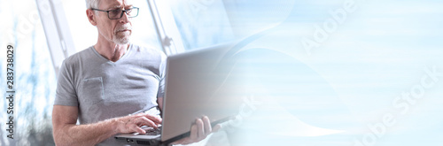 Senior businessman standing and working on his laptop; panoramic banner