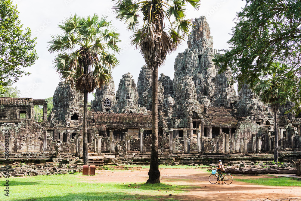 Young woman riding bicycle next to Bayon temple in Angkor Wat complex, Cambodia
