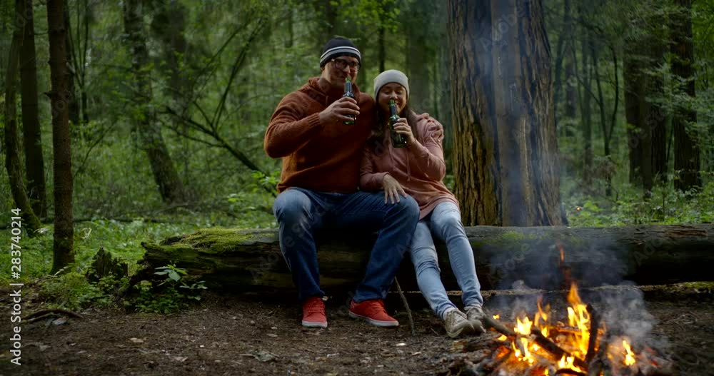 cheerful middle-aged couple relaxing on a weekend camping in the woods with a fire and drink beer from the bottle cheerful middle-aged couple relaxing on a weekend camping in the woods with a fire and drink beer from the bottle
