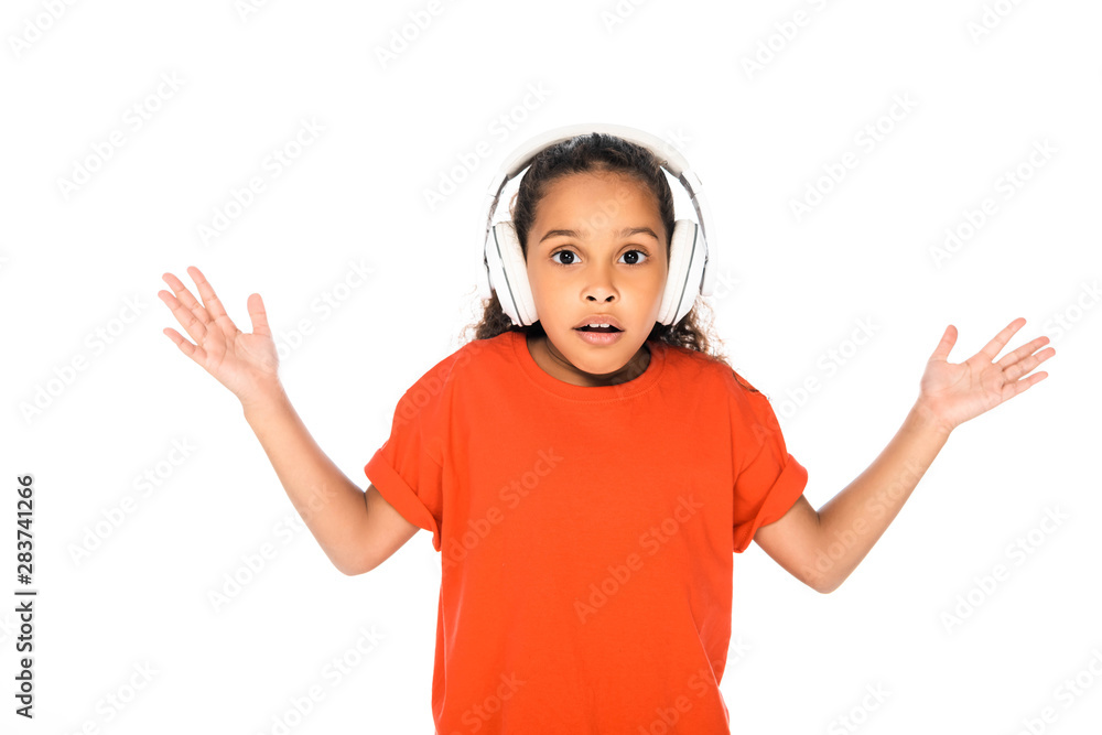 surprised african american kid showing shrug gesture while listening music in headphones isolated on white surprised african american kid showing shrug gesture while listening music in headphones isolated on white