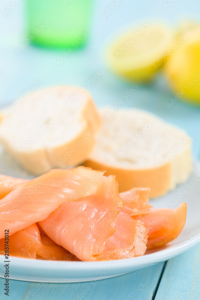Smoked salmon slices with baguette on blue plate, lemon and glass in the back, photographed on blue wood (Selective Focus, Focus one third into the image) Smoked salmon slices with baguette on blue plate, lemon and glass in the back, photographed on blue wood (Selective Focus, Focus one third into the image)