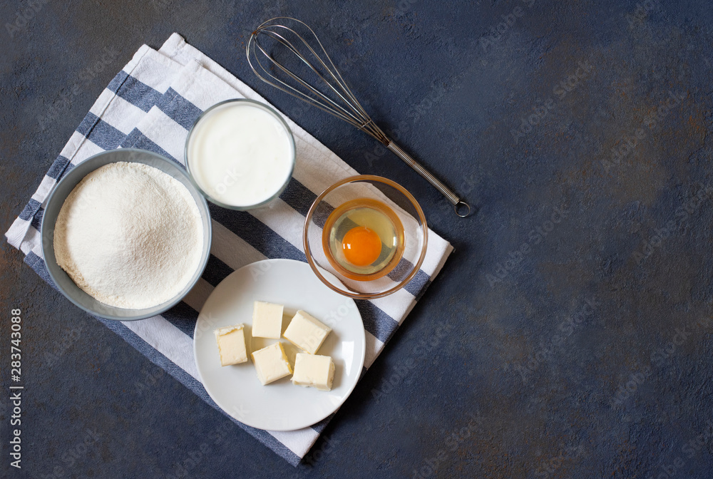 Ingredients for crepes and pancakes on a dark background. Flour, egg, milk, butter, whisk. Top view. Space for text Ingredients for crepes and pancakes on a dark background. Flour, egg, milk, butter, whisk. Top view. Space for text