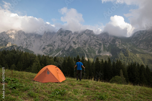 Male hiker standing near his trekking tent on a green and beautiful mountain landscape. Adventure travel lifestyle concept