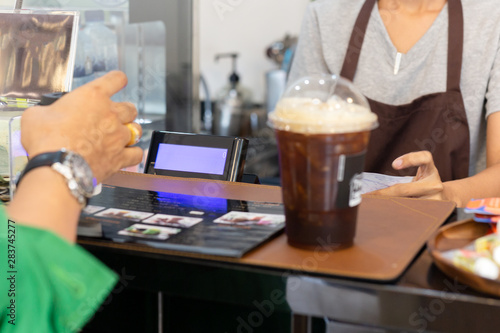 Woman barista serving iced coffee to customer at counter bar in cafe.