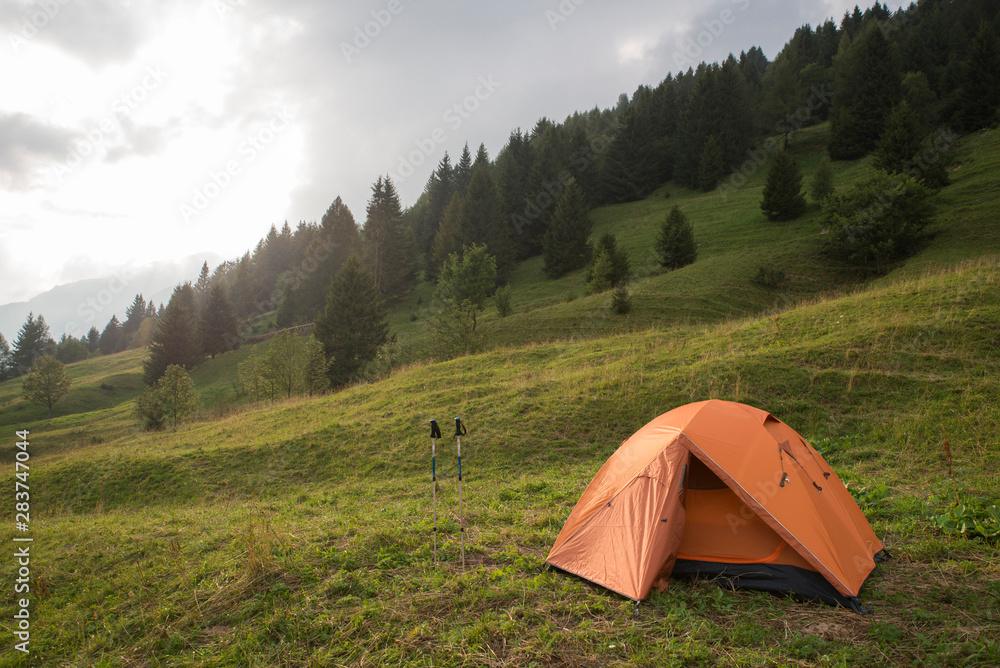 Beautiful early morning camping view. Mountain meadow landscape with an orange trekking tent
