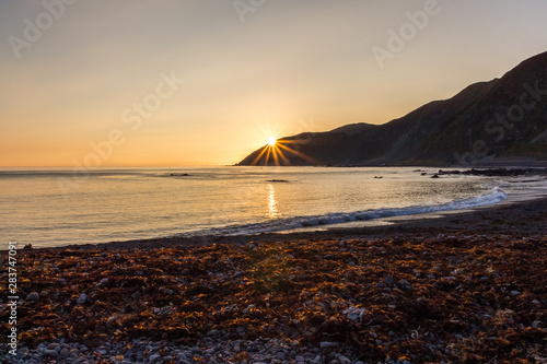 Beautiful sunset at the beach of Wellington in New Zealand Nort Island with sun star right above the moutains
