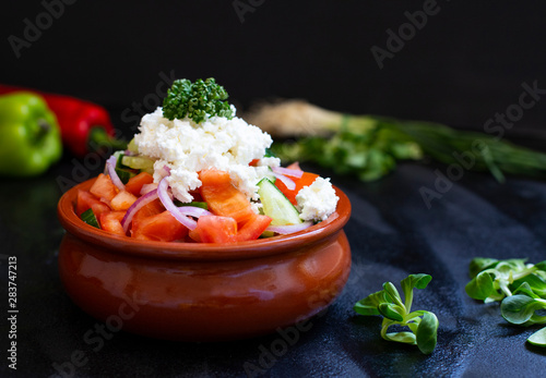 Traditional shopska salad with fresh vegetables and cheese. Traditional Balkan, Serbian, Bulgarian, Macedonian cuisine. Two plates of salad. Black background. Close-up view