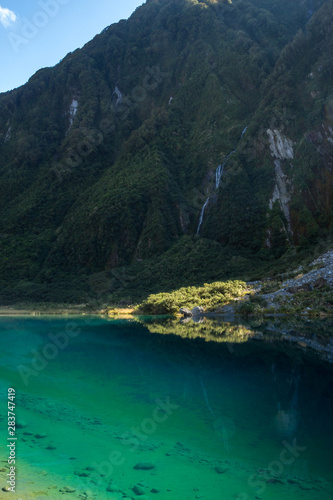 Beautiful green and blue lake with waterfall near glacier Franz Josef in New Zealand South Island