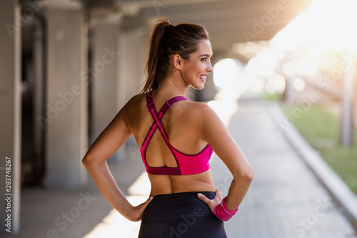 Young sporty woman training. Woman Doing Workout Exercises On Street. Beautiful Athletic Fit Girl In Bright Sports Clothing Stretching Her Arms And Relaxing After Fitness Training On Street.